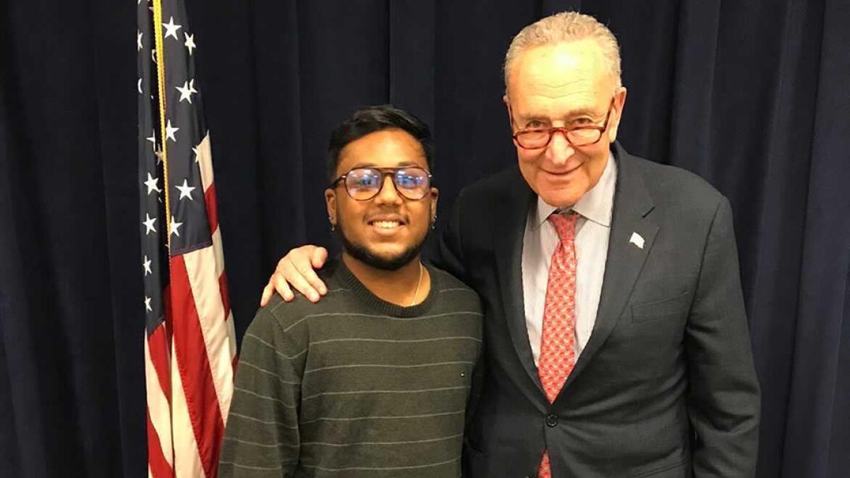 Student Aman Islam stands in front of an American flag with Senate Majority Leader Charles Schumer
