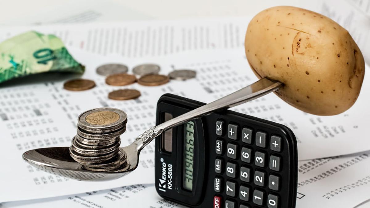 currency bills, coins, potato, and spoon balanced on calculator representing the concept of "inflation"