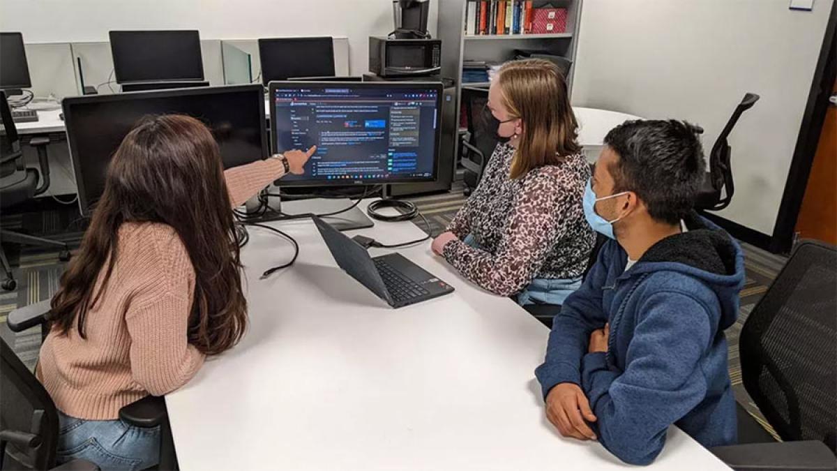 Three students gather around a computer screen.