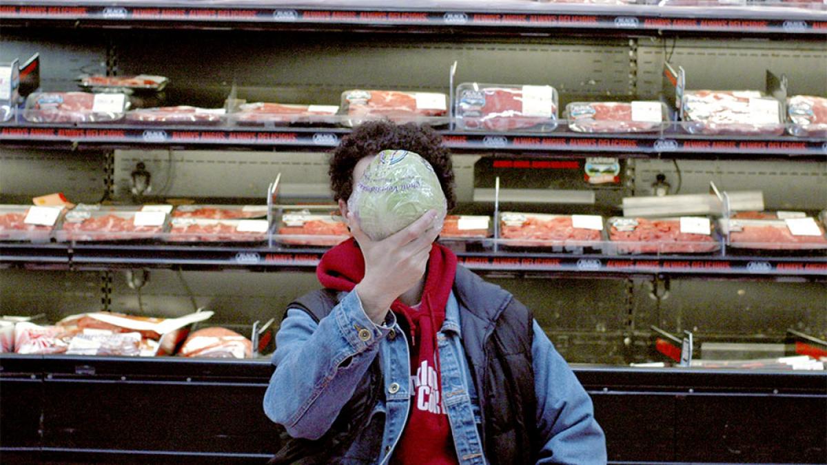 Person in food store with lettuce in front of their face.