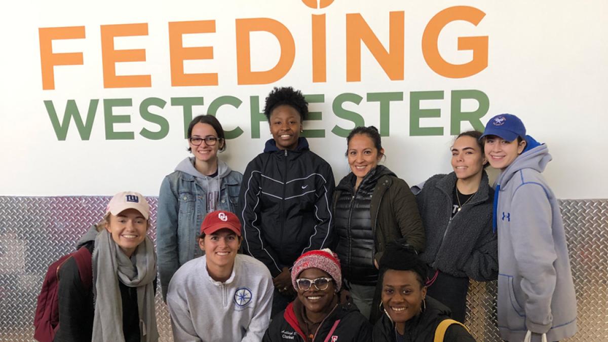 Students smile in front of a sign that says "Feeding Westchester"