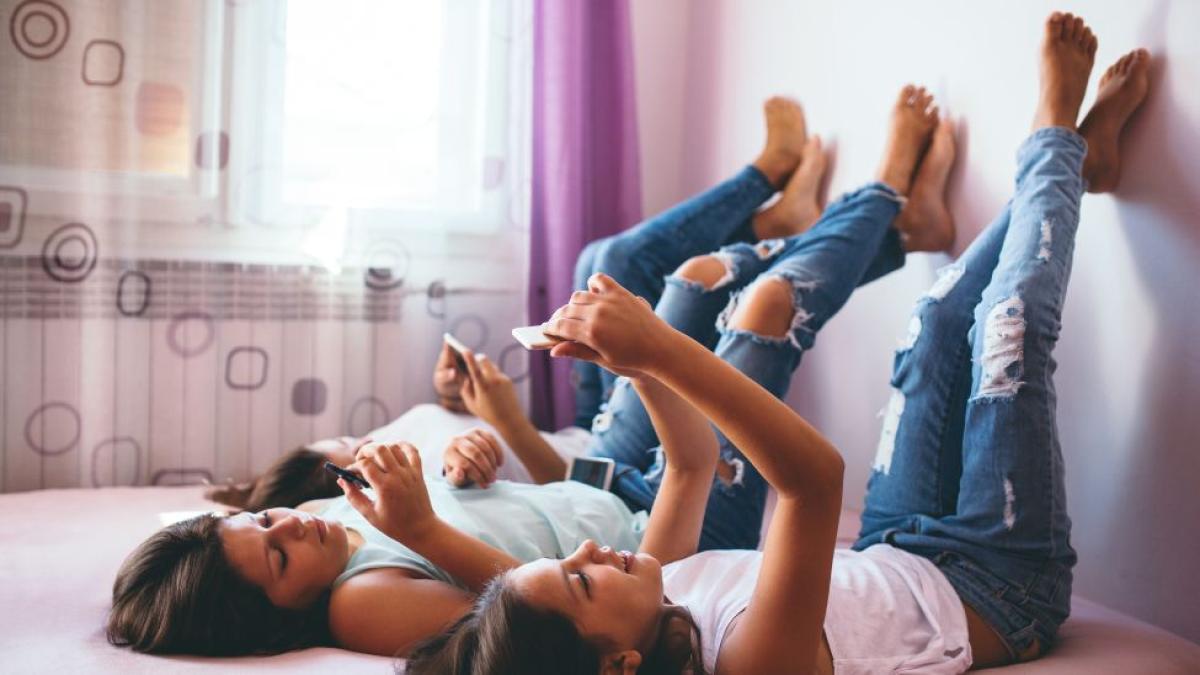 teen girls laying down feet up on wall looking at their cell phones