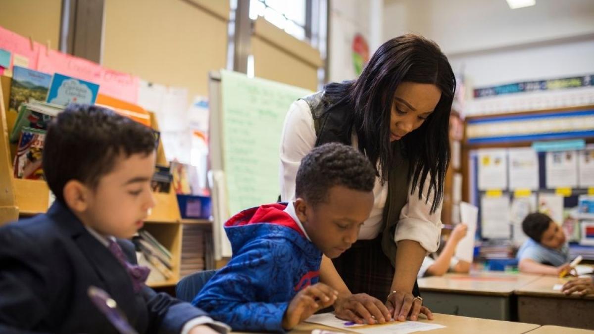 Teacher showing student work at desk in classroom