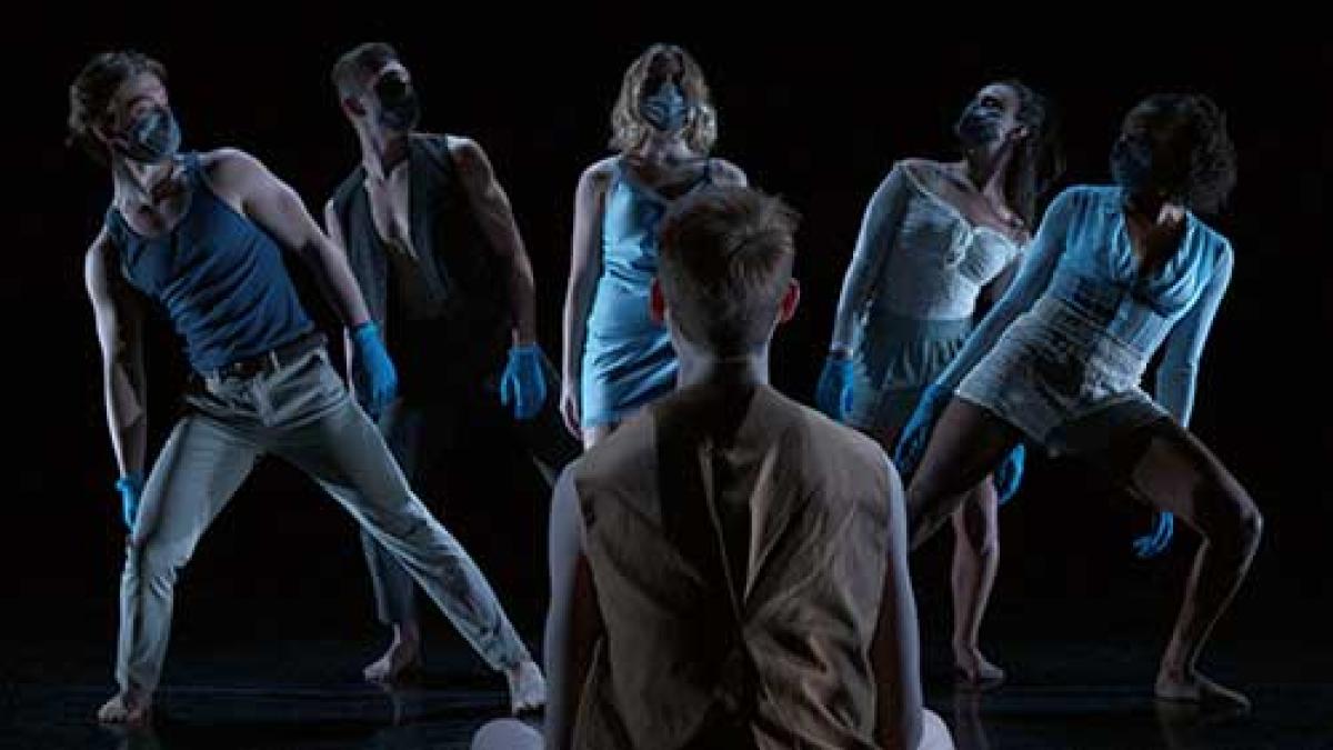 dancers on a darkened stage wearing masks.