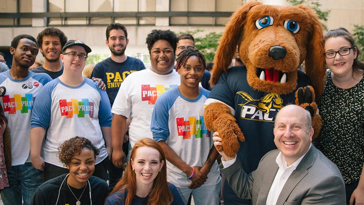 Presiden Krislov smiling at the camera, standing with a group of students and T-Bone, Pace's mascot.