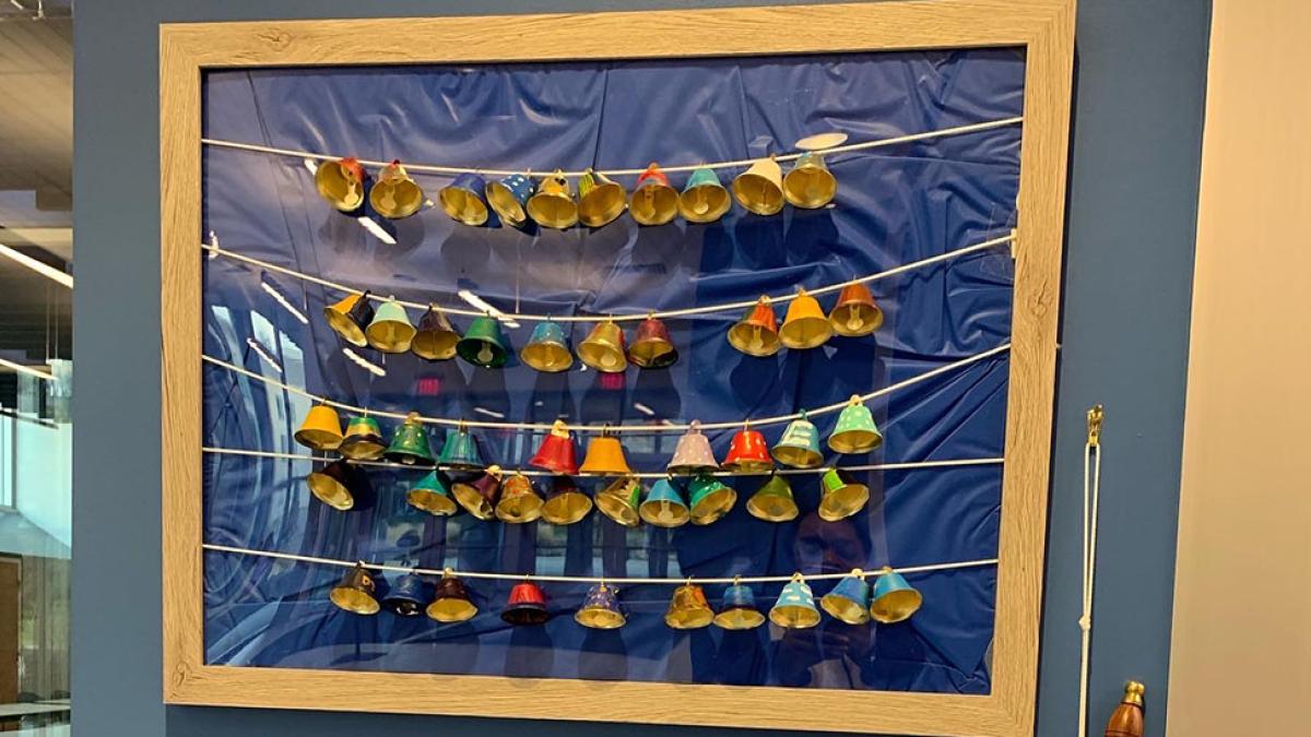 50 colorfully painted bells strung together on string, pinned to a blue background 