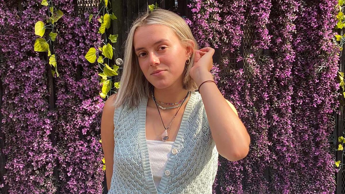 Student Danielle Harari stands in front of a wall of purple flowers
