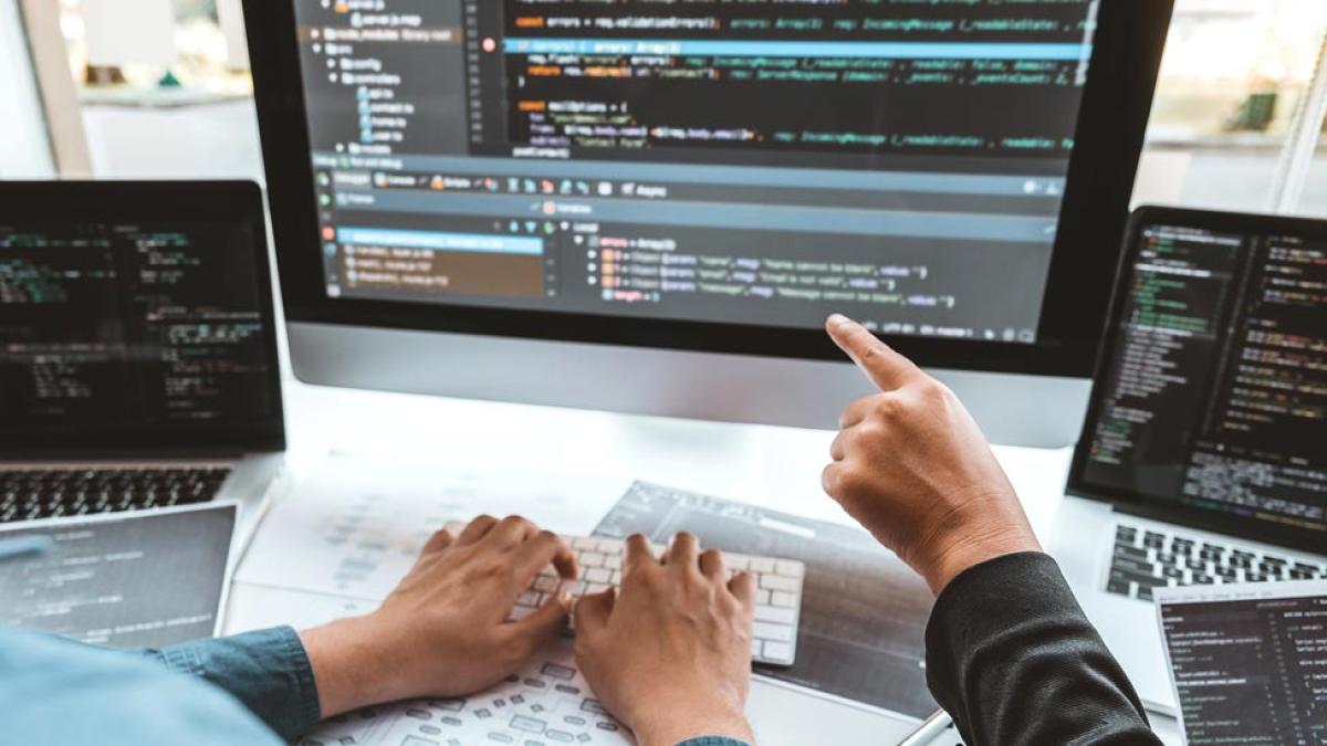 Two individuals pointing to computer code on screen