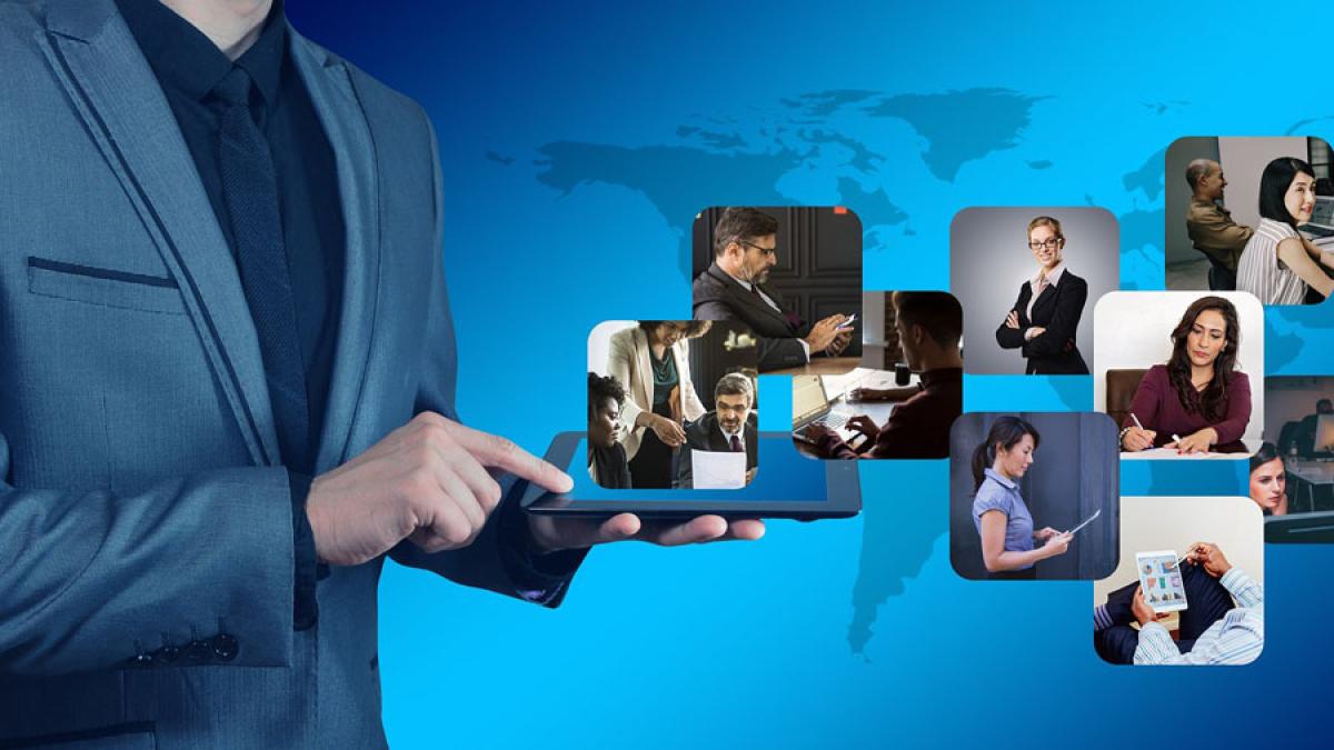 man in business attire using the touch screen of a tablet with boxed images of various people floating above the tablet against a world map background to represent the concept of "collaboration"