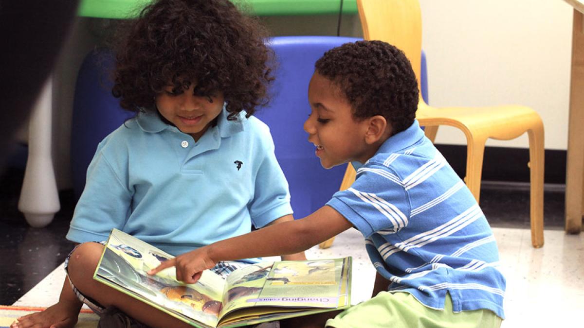 two preschool aged children reading a book.