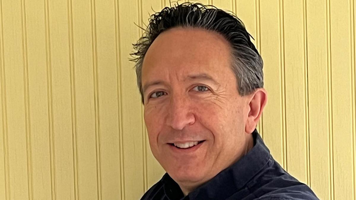 man smiling for camera in front of yellow panel wall