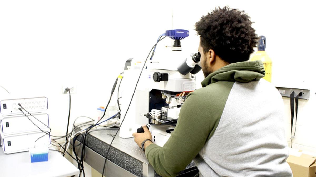 Male in a hoodie looking through a high-powered microscope