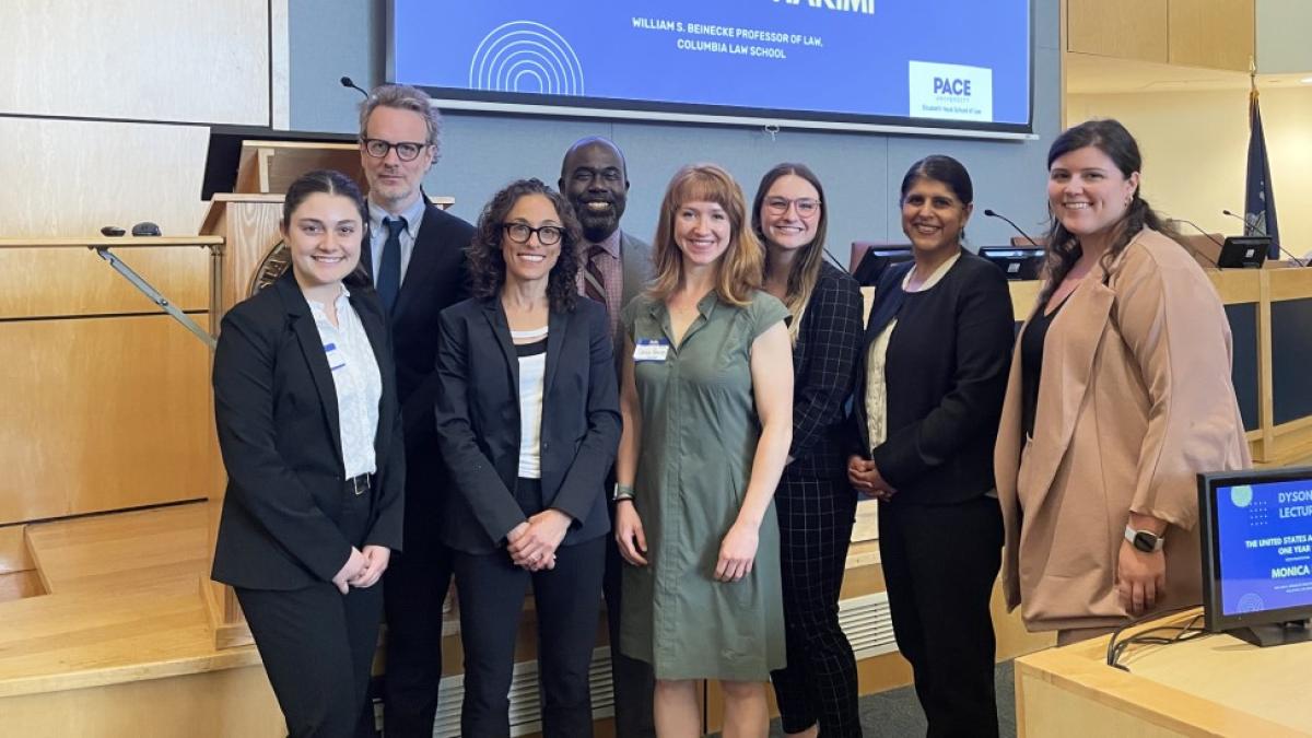 Panelists, Professors, and Students standing in front of podium in lecture hall