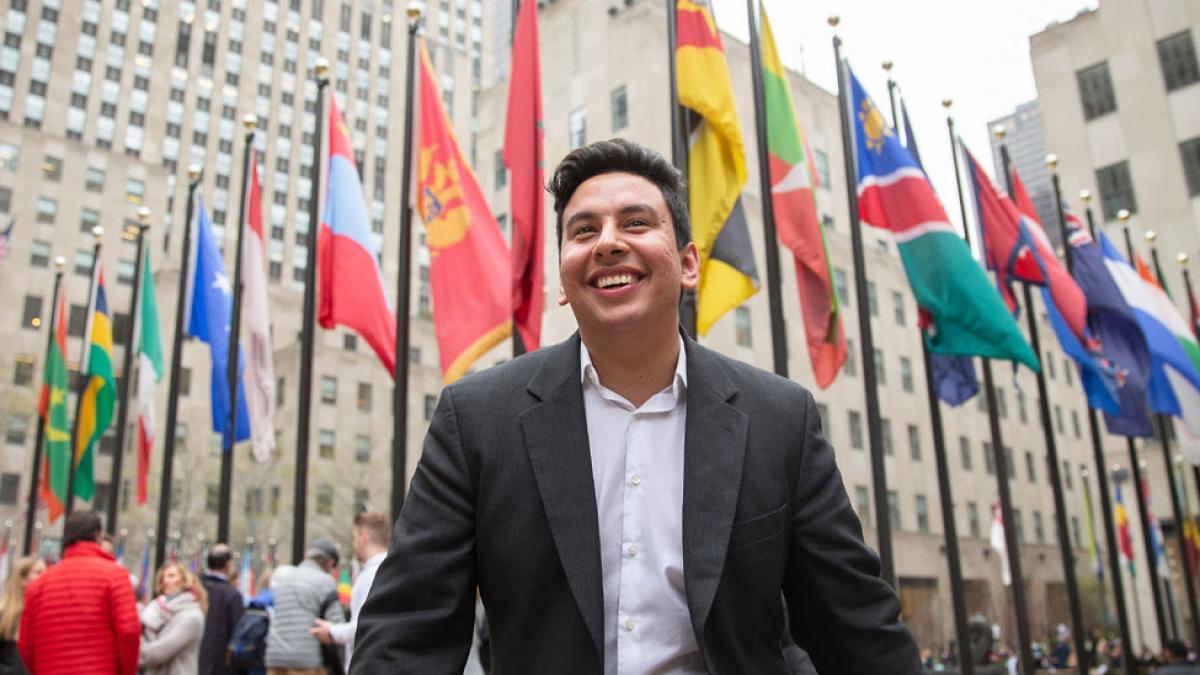 young man in business casual attire standing in front of the Manhattan United Nations row of international flags
