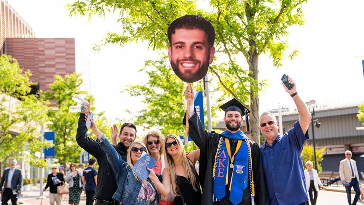 pace graduate and family holding a sign with the graduate's face printed on it. 