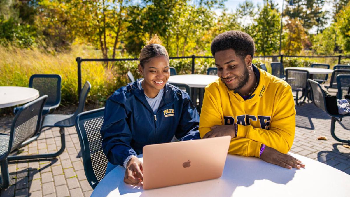 two pace students sitting outside looking at a laptop while on the pleasantville campus