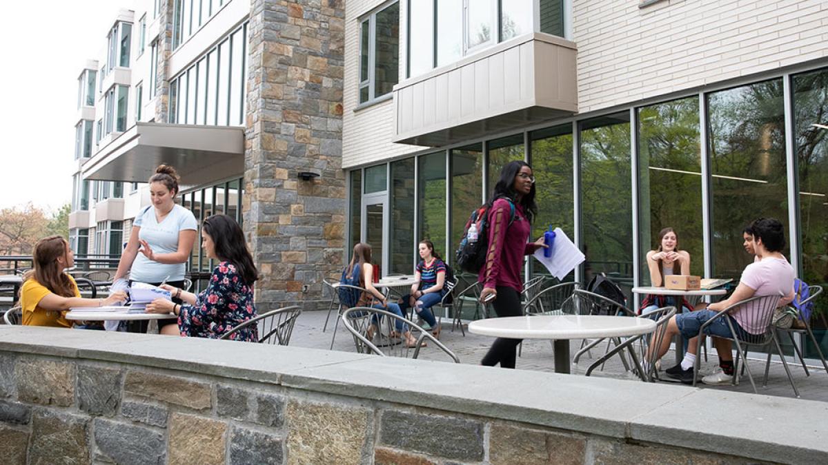 Several pace university students sitting at tables on a patio outside a residential building