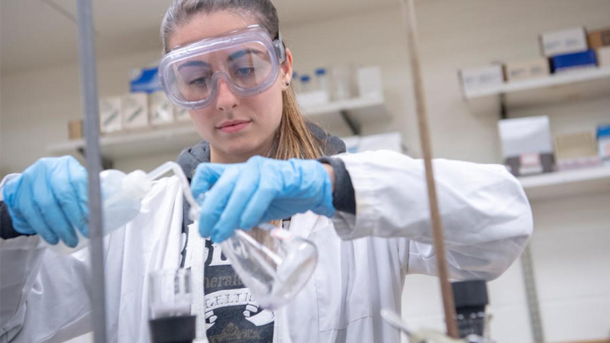 Female wearing gloves pouring chemicals in a lab