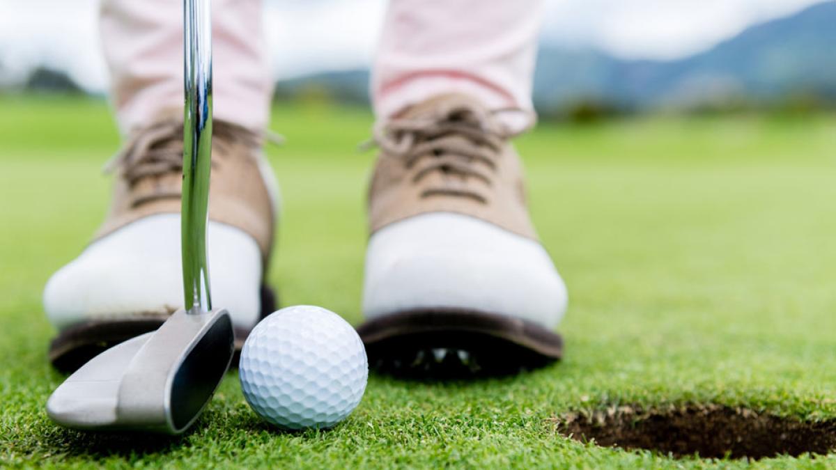 close up of golf shoes with golf club and golf ball