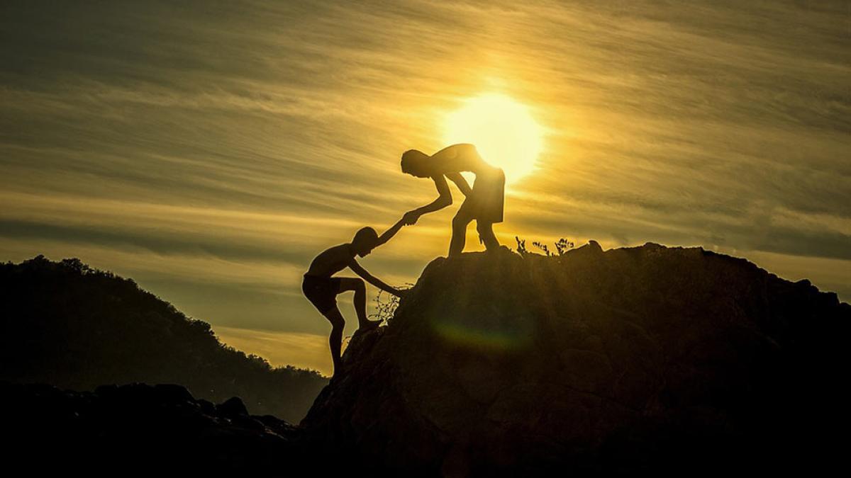 Silhouettes of two men climbing a mountain