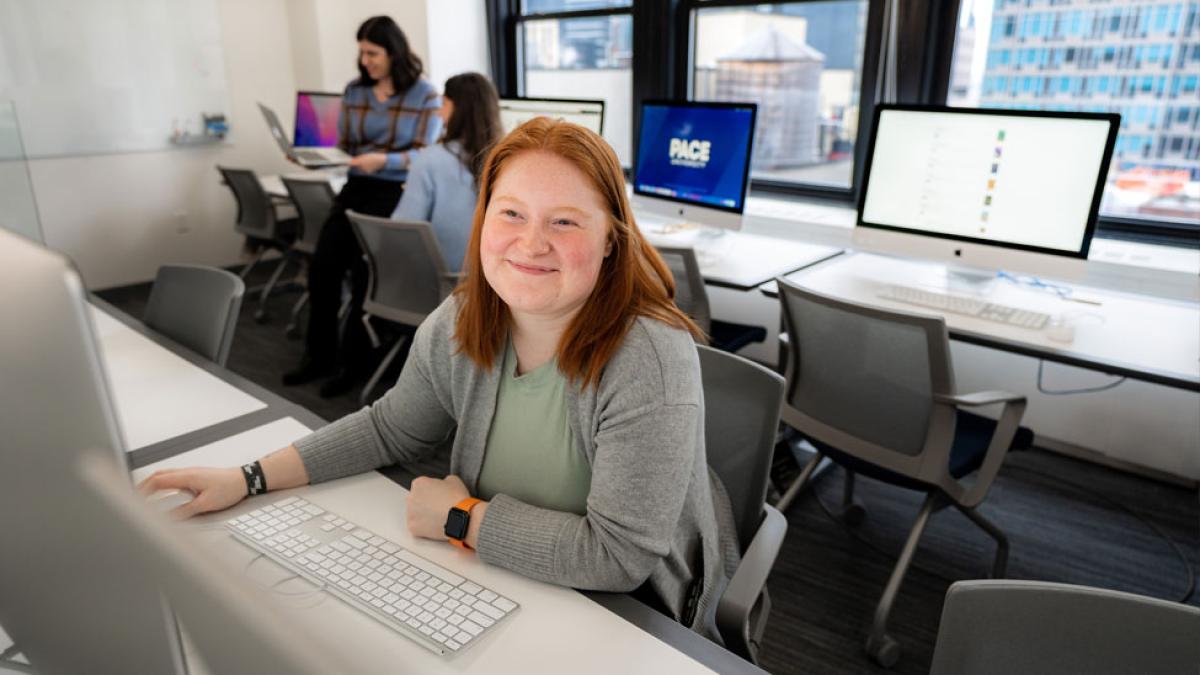 pace student sitting at a computer and smiling at the camera