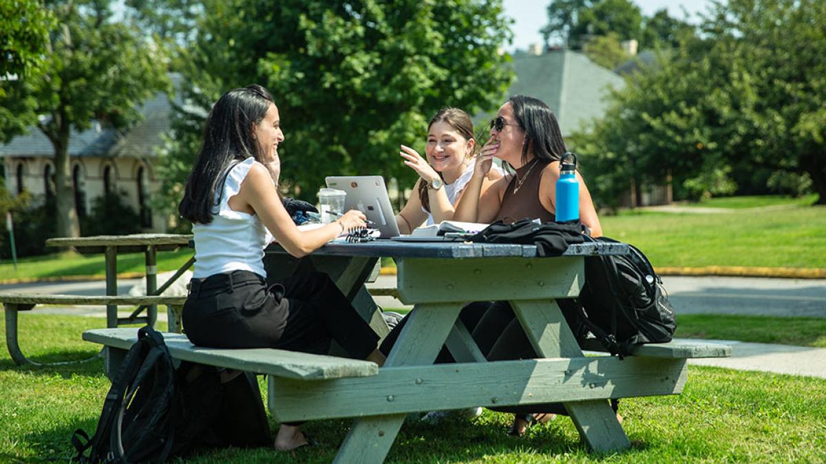 Three Pace University students sitting at a picnic table on the Elisabeth Haub School of Law campus.
