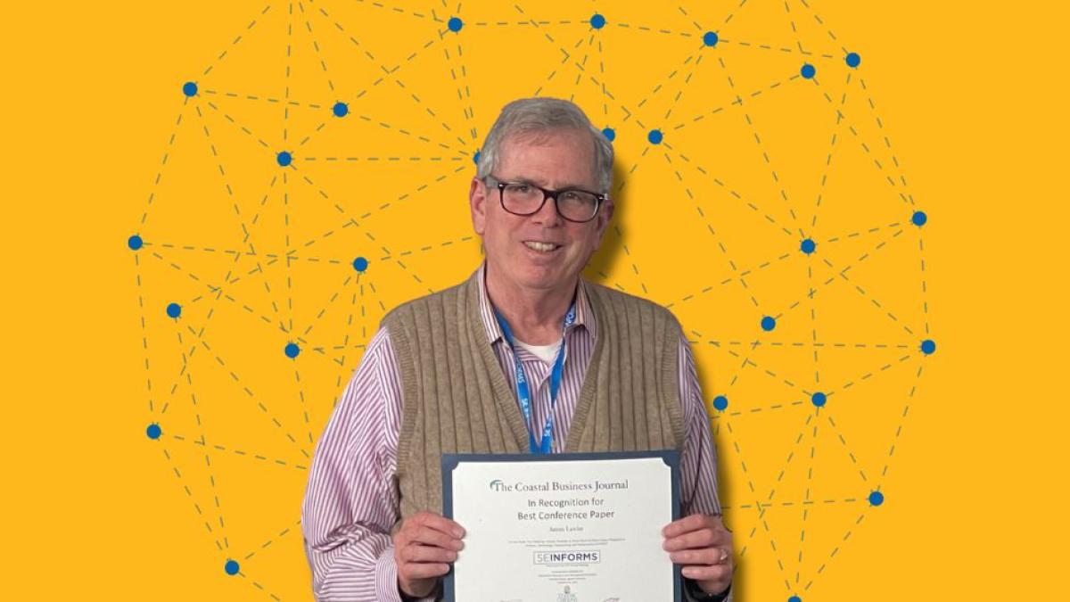 Dr James Lawler on a yellow graphic background holding a certificate for best paper at a conference