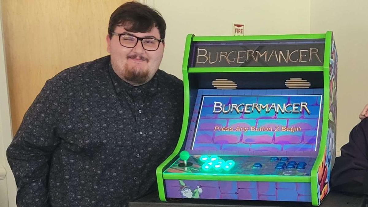 Seidenberg student Michael Falco beside his hand-built arcade game, BurgerMancer