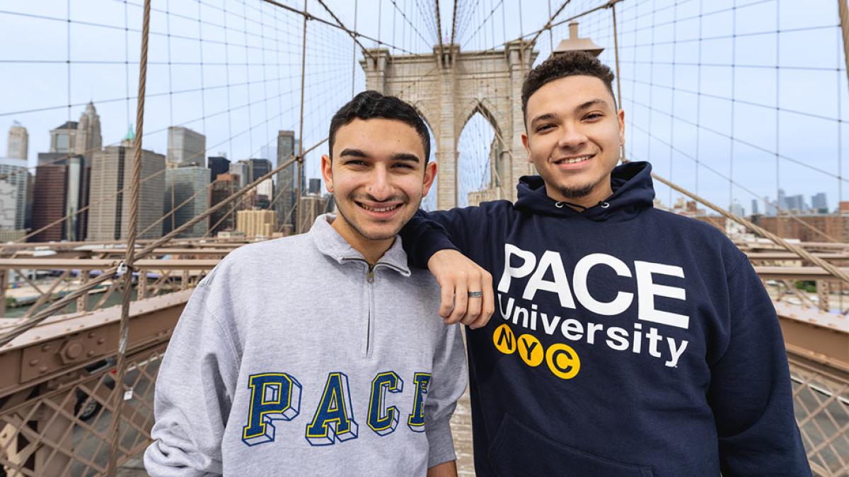 two people in pace university sweatshirts posing on the brooklyn bridge.