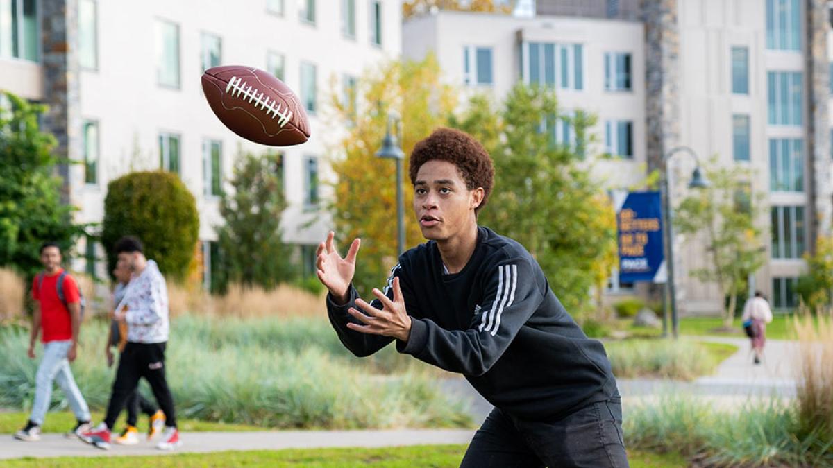 Pace university student catching a football on campus.