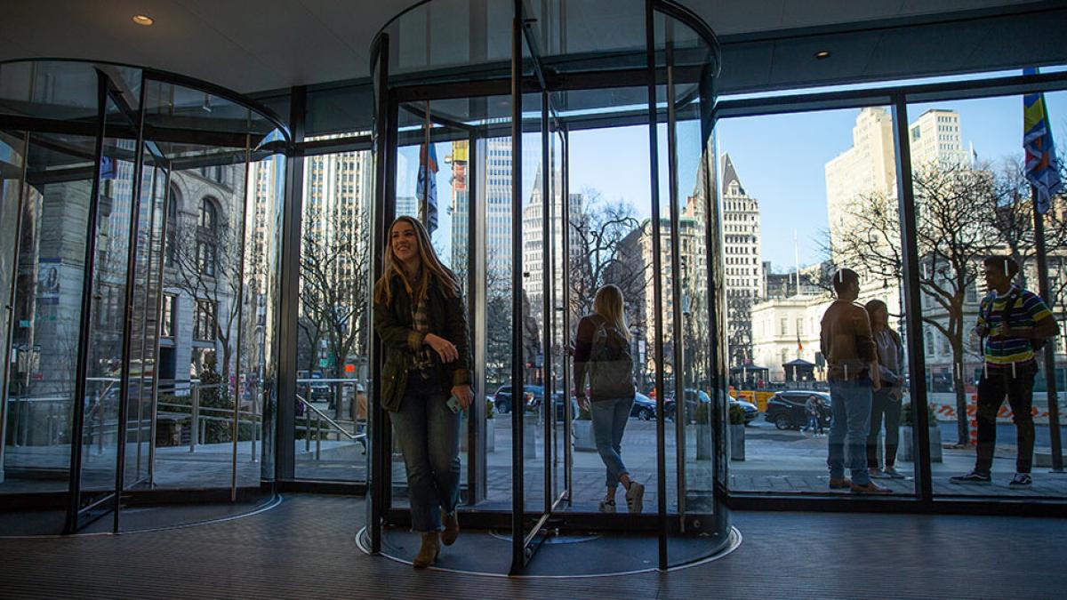 Pace University student walking through a revolving door on the NYC campus.