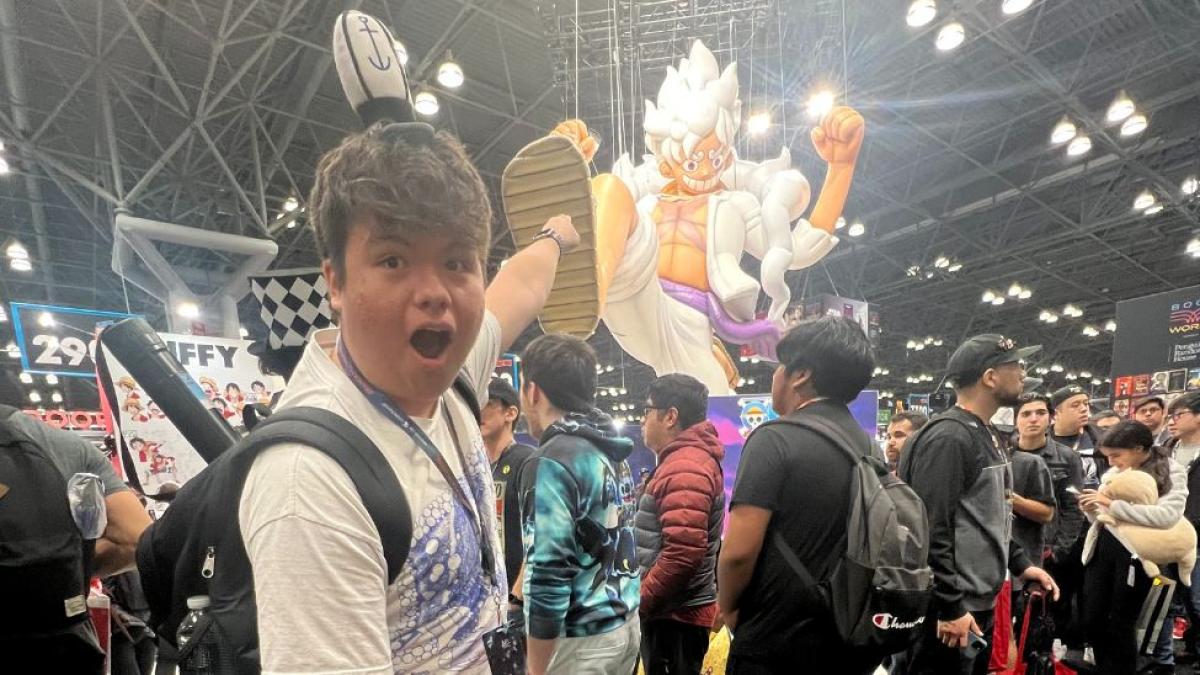 Pace student Daniel Ramos standing at a Comic Con convention in NYC, and pointing at a large anime character.