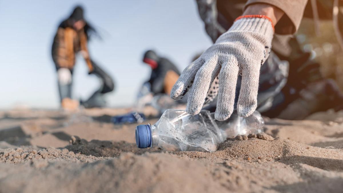 A hand picking up trash on a beach