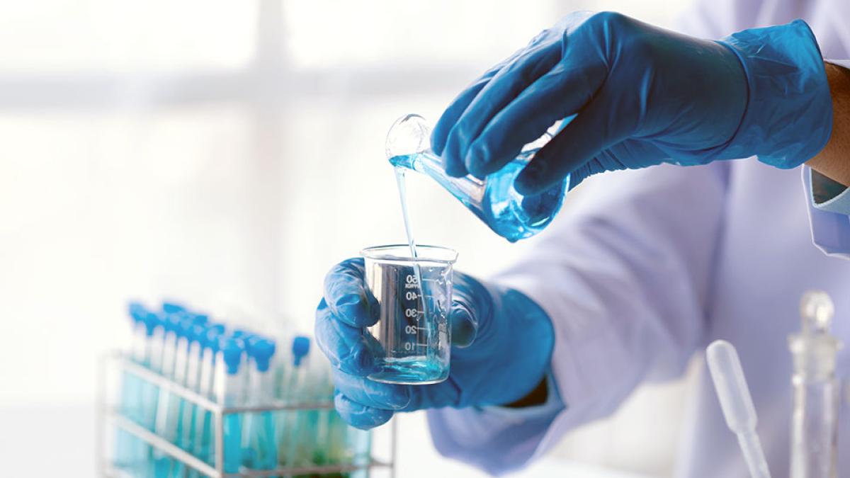 Gloved hands pouring a chemical solution into a beaker