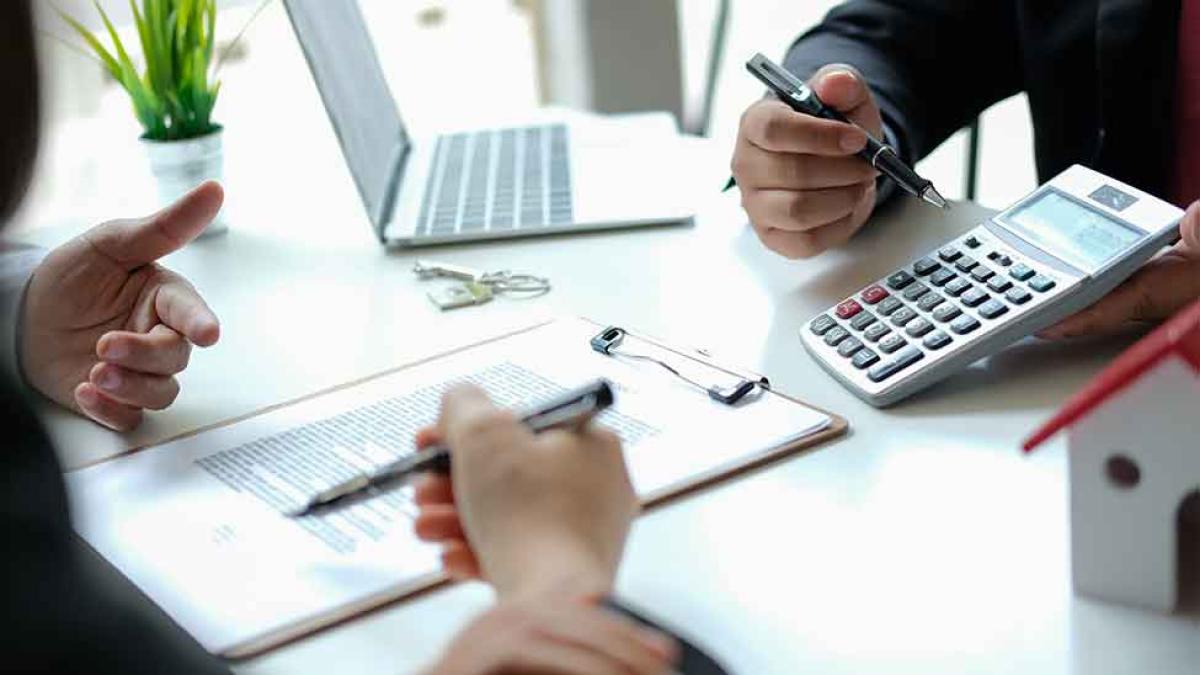 Two people sitting at a desk with a laptop, calculator and notepad.