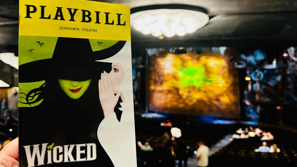 A hand holding a playbill for Wicked inside the theater. 