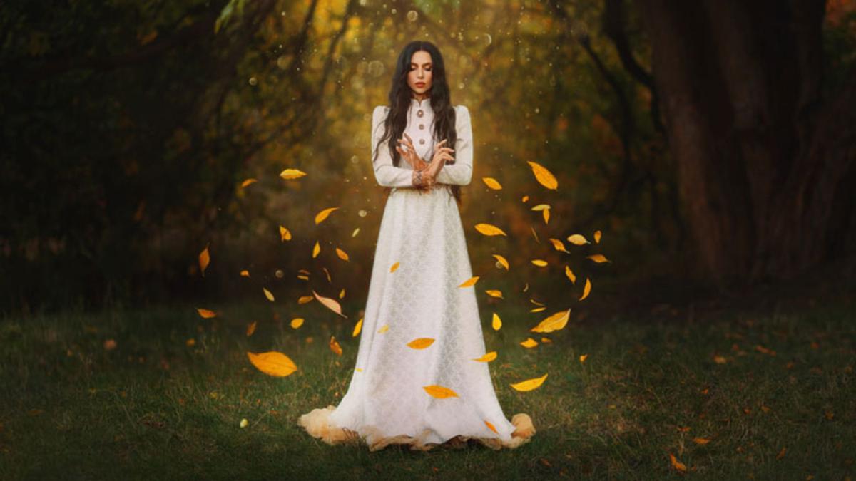 A woman in the woods with leaves swirling around her.