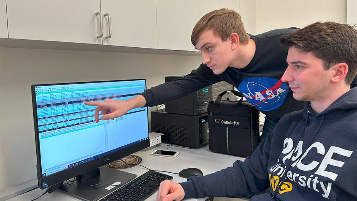 Pace student Steven Schiavone gestures to a computer for another Pace student