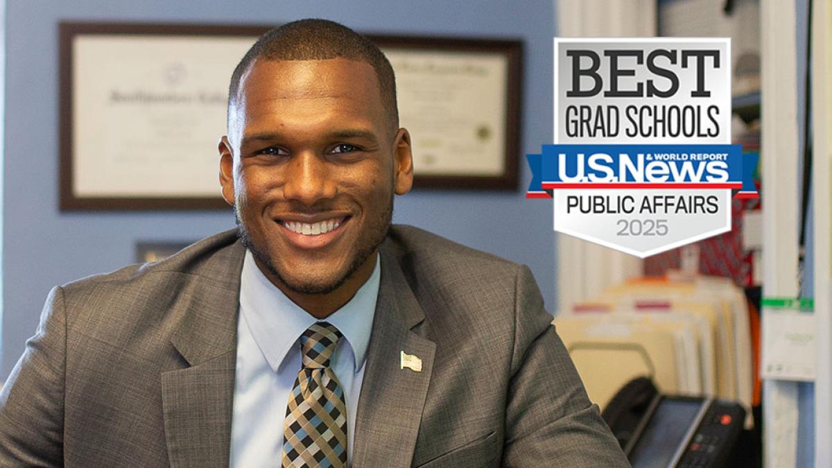 A male public administration graduate in an office with a badge from US News and World Report that says Best Grad Schools for Public Affairs