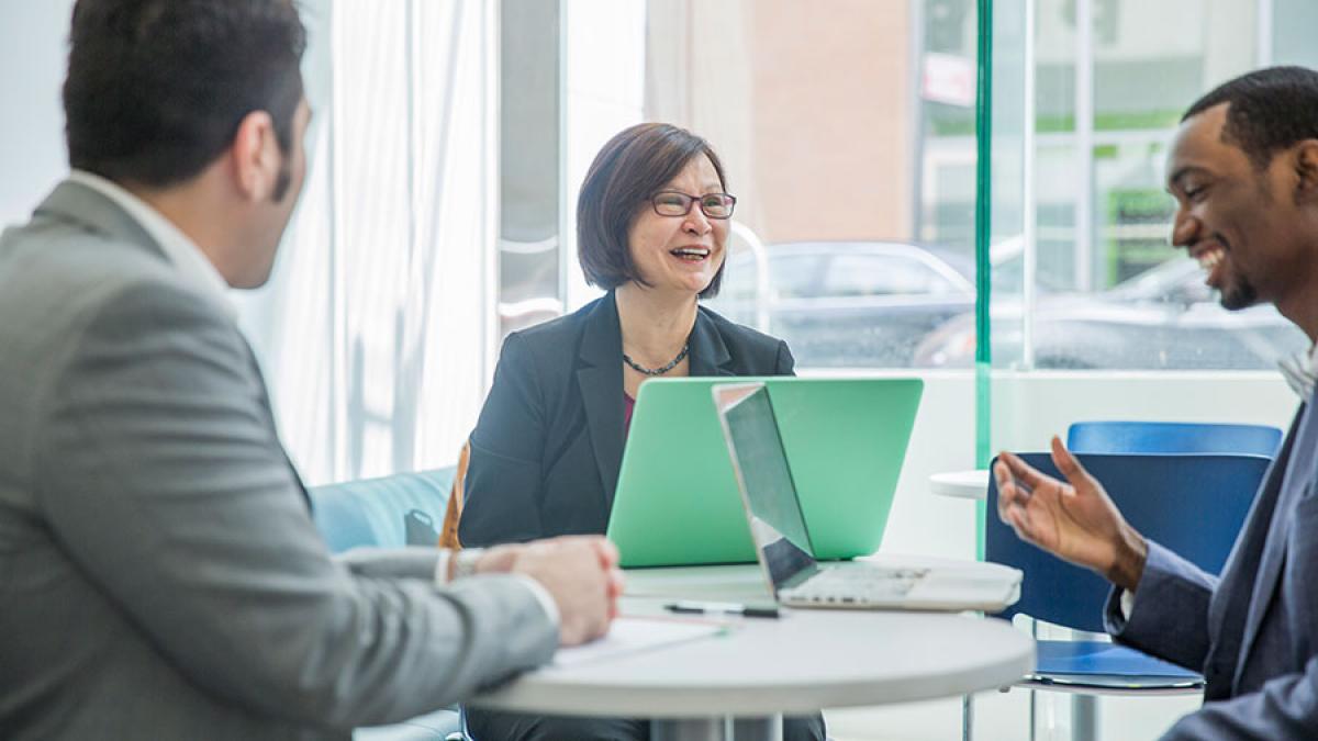 Group of people in business casual attire, sitting around a desk at work.