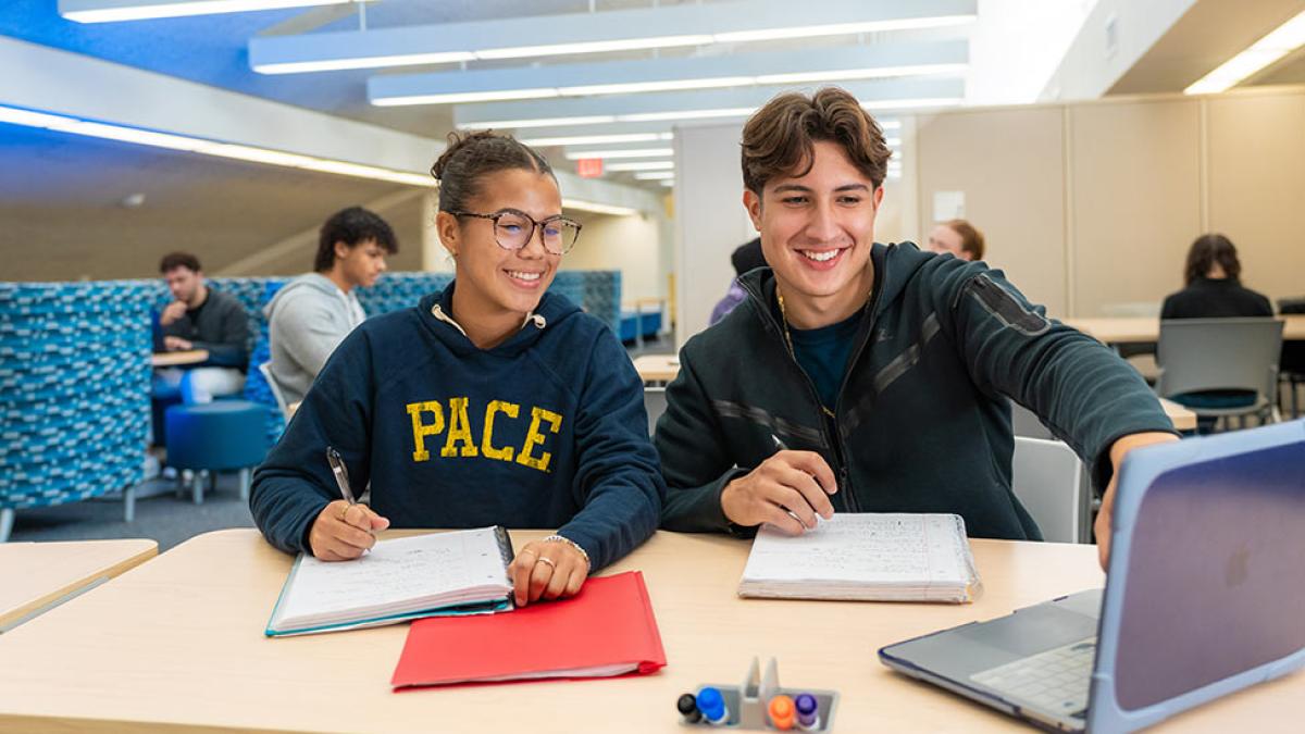 Two Pace University students working on a project on a laptop in the library.