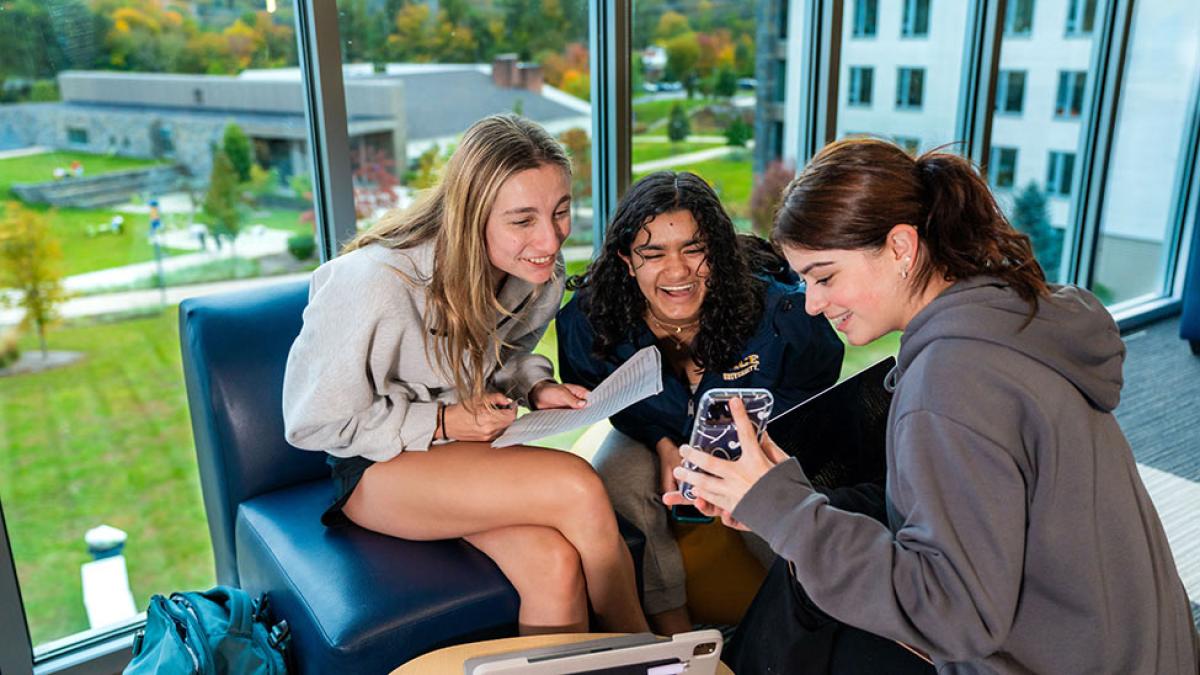 Three Pace University students laughing while looking at a photo on a cell phone.