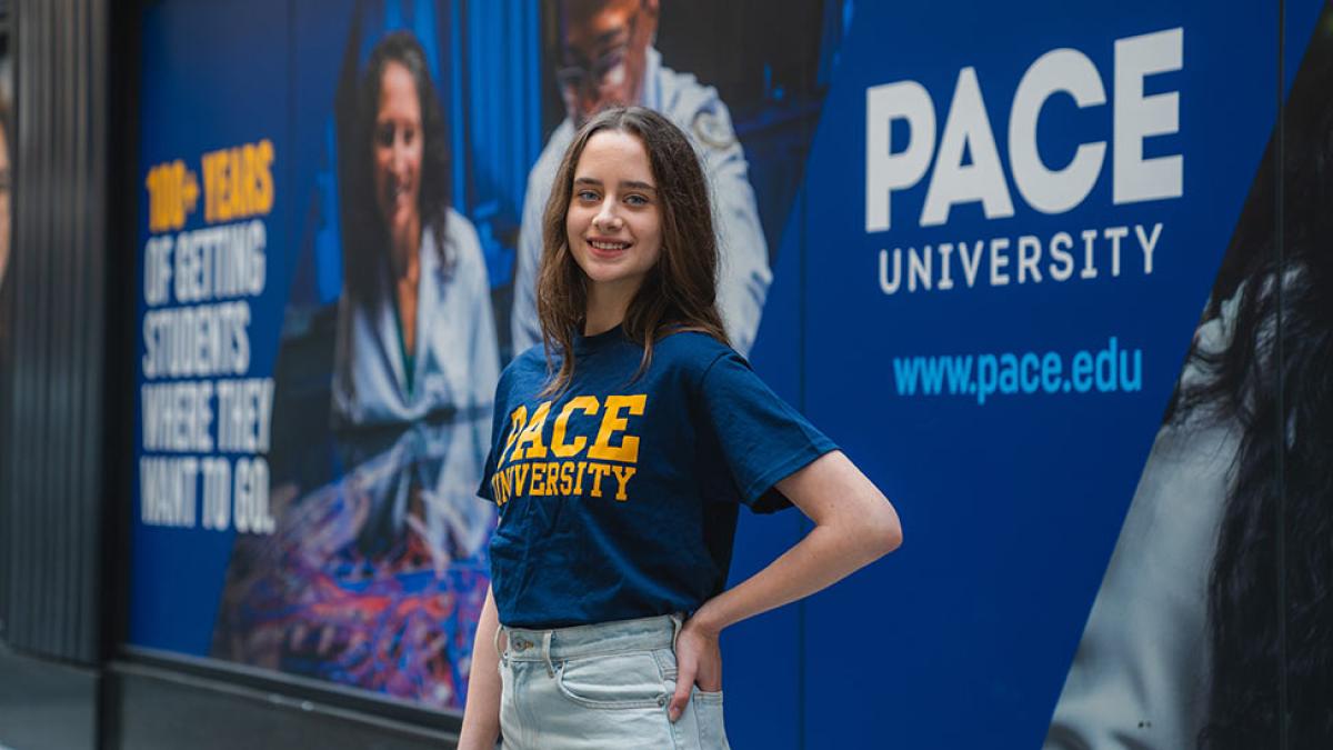 Student posing in front of a Pace University ad in New York City.