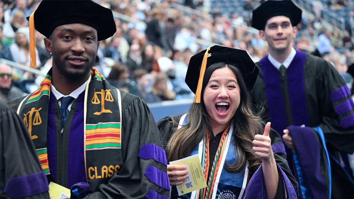 Three excited graduating law students with an Asian girl giving thumbs up and a black male smiling at the camera
