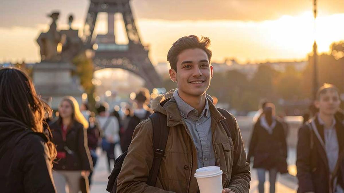 Student standing in front of Eiffel Tower holding a coffee and smiling