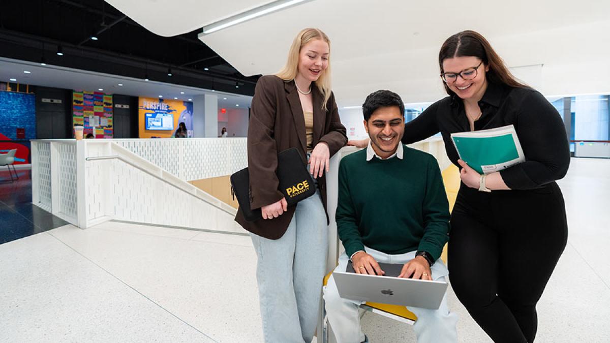 Three Pace University students gather around a laptop