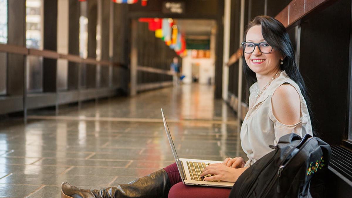 Pace University student sitting in a school hallway working on a computer.