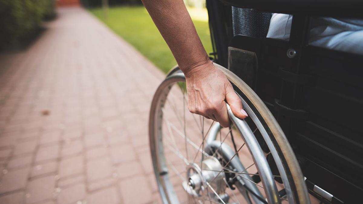 Side angle of a person in a wheel chair with their hand on the wheel.