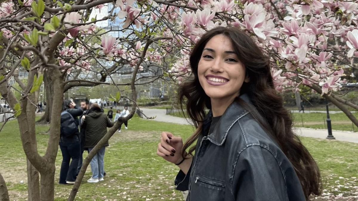Seidenberg student Daisy Molina posing for a photo in front of cherry blossom trees.