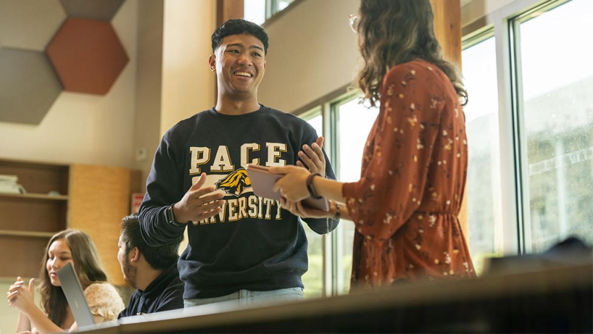 A student in a classroom talking with a professor.